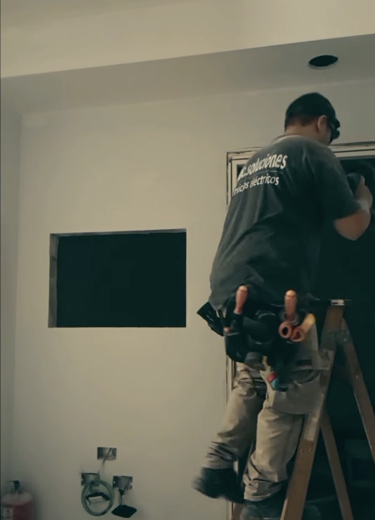Bruno Cabrera instalando un artefacto eléctrico arriba de una escalera